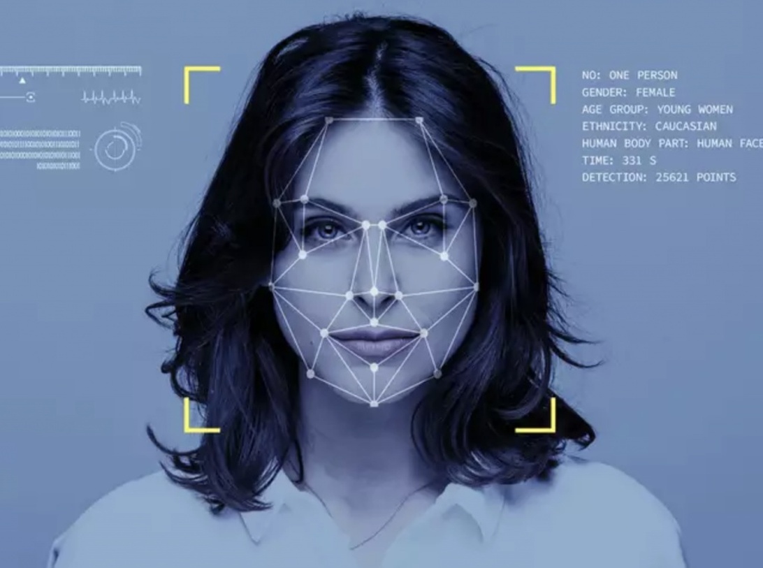 Et ansigtsgenkendelsessystem scanner en persons ansigt med et blåt geometrisk overlay, hvilket repræsenterer teknologiske løsninger til sikkerhedsrisikostyring.